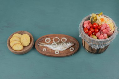 Haşlanmış patates dilimleri, ringa balığı ve ahşap domates kovası, sarımsak, lahana, mavi masada salatalık. Yüksek kalite fotoğraf