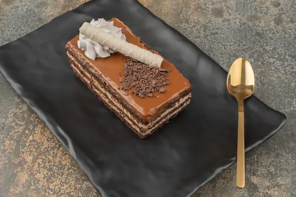 Koyu tabakta altın kaşıkla bir dilim pasta. 