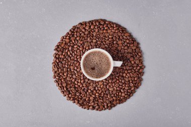 Gri arkaplanda kahve çekirdekleri olan bir fincan kahve.