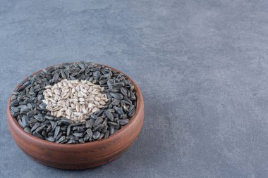 Kabuğu soyulmuş ve soyulmamış ayçiçeği tohumları tahta kasede, mermer arka planda. Yüksek kalite fotoğraf