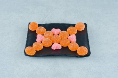 Pembe kalp şeklinde marmelatlı turuncu şekerlerle dolu siyah bir tabak. Yüksek kalite fotoğraf