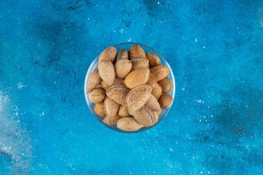 Mavi arka planda cam bir kase kabuklu badem. Yüksek kalite fotoğraf