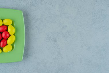 Beyaz arka planda tatlı sarı ve kırmızı şekerli yeşil bir tabak. Yüksek kalite fotoğraf