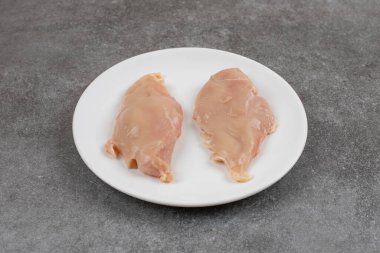 Gri arka planda beyaz seramik tabakta taze çiğ tavuk göğsü. Yüksek kalite fotoğraf