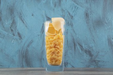 Mavi arka planda cam içinde iki çeşit çiğ makarna. Yüksek kalite fotoğraf