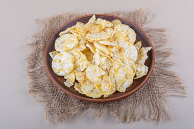 Kahverengi tabak beyaz masa üzerinde gevrek pirinç cipsi.