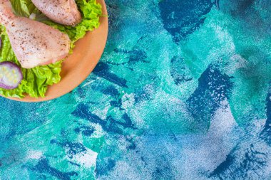 Mavi arka planda, kilden bir tabakta soğan marulu ve tavuk budu. Yüksek kalite fotoğraf