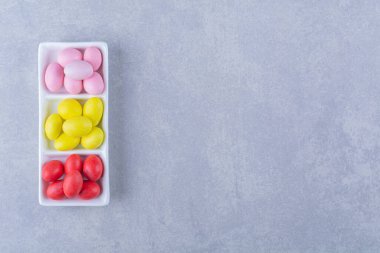 Gri arkaplanda renkli fasulye şekerleriyle dolu beyaz bir tahta. Yüksek kalite fotoğraf