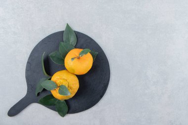 Siyah kesme tahtasında yaprakları olan iki olgun mandalina. Yüksek kalite fotoğraf