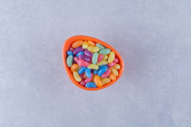 Gri arkaplanda renkli fasulye şekerleriyle dolu turuncu bir tabak. Yüksek kalite fotoğraf