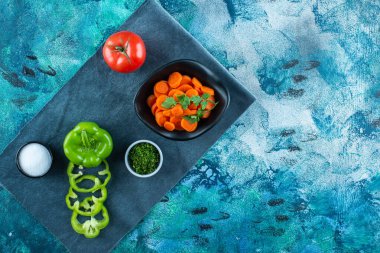 Havlunun üzerinde, mavi arka planda sebzelerin yanında bir kasede dilimlenmiş havuç. Yüksek kalite fotoğraf