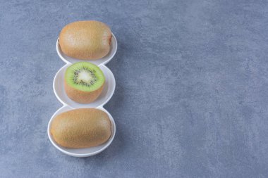 Mermer arka planda, bir tabakta tam ve yarım kivi meyvesi. Yüksek kalite fotoğraf