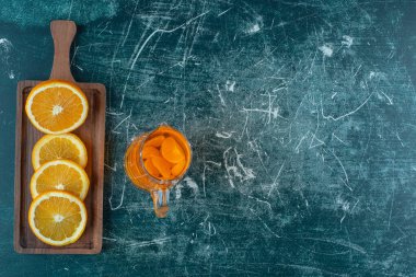 Olgun portakallı bir tahta üzerinde, mermer kaplamalı sürahi meyve suyunun yanında. Yüksek kalite fotoğraf