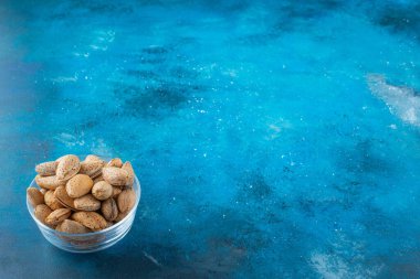 Mavi arka planda cam bir kase kabuklu badem. Yüksek kalite fotoğraf