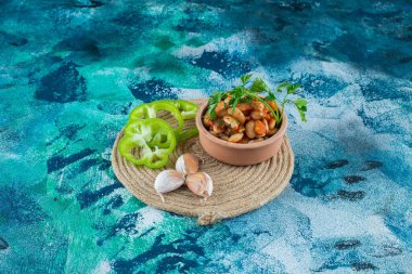 Bir kase fırında fasulye, maydanozlu, sarımsağın yanında bir biber, mavi arka planda. Yüksek kalite fotoğraf