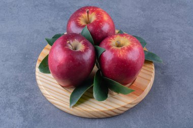 Ahşap tabakta kırmızı elmalar ve yapraklar mermer arka planda. Yüksek kalite fotoğraf