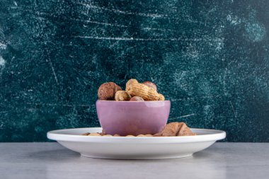 Taş zeminde çeşitli kabuklu cevizlerle dolu mor bir kase. Yüksek kalite fotoğraf