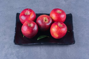 Ahşap tabakta, mermer zemin üzerinde olgun kırmızı elmalar. Yüksek kalite fotoğraf
