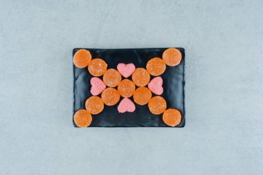 Pembe kalp şeklinde marmelatlı turuncu şekerlerle dolu siyah bir tabak. Yüksek kalite fotoğraf