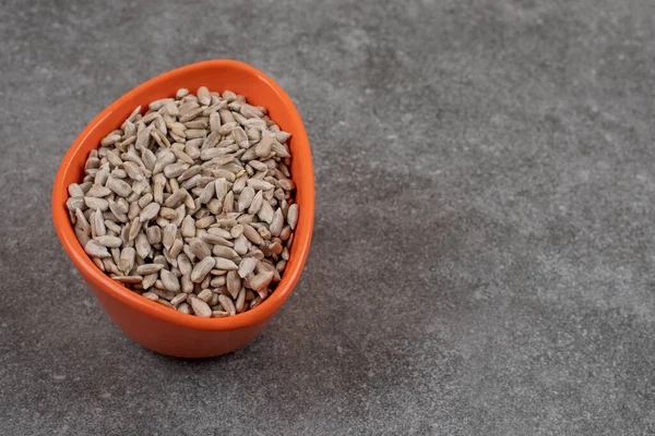 Peeled sunflower seeds in orange bowl over grey background. High quality photo