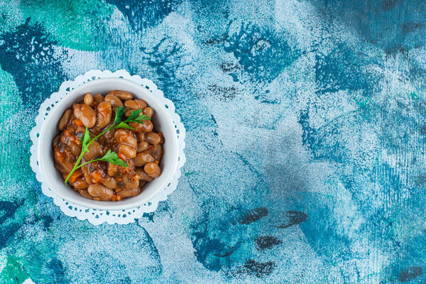 Чаша с запечённой фасолью на подставке, на синем фоне. Высокое качество фото