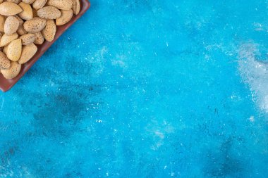 Kabuklu bademler bir tabakta, mavi arkaplanda. Yüksek kalite fotoğraf