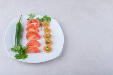 Havuçta kırmızı biber, tabakta domateslerin yanında, mermer zemin üzerinde. Yüksek kalite fotoğraf