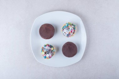 Mini tart kekleri ve çikolata kaplı kurabiyeler bir tabakta, mermer arka planda. Yüksek kalite fotoğraf