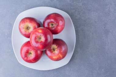 Elmalar tabakta üst üste istiflenmiş, mermer zeminde. Yüksek kalite fotoğraf
