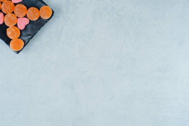 Pembe kalp şeklinde marmelatlı turuncu şekerlerle dolu siyah bir tabak. Yüksek kalite fotoğraf