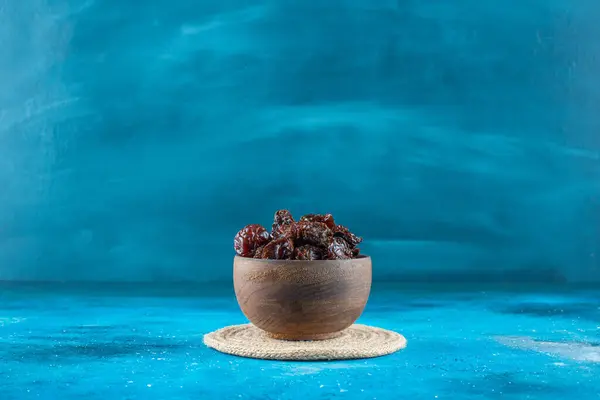 A bowl of dried plums on a trivet , on the blue background. High quality photo