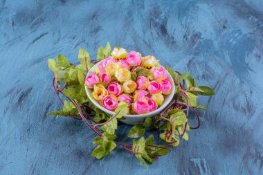 Mavi arka planda yapay renkli güller olan bir kase. Yüksek kalite fotoğraf