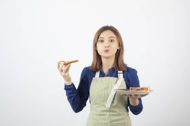 Kadın aşçı önlüklü, elinde pizza, kameraya bakıyor.