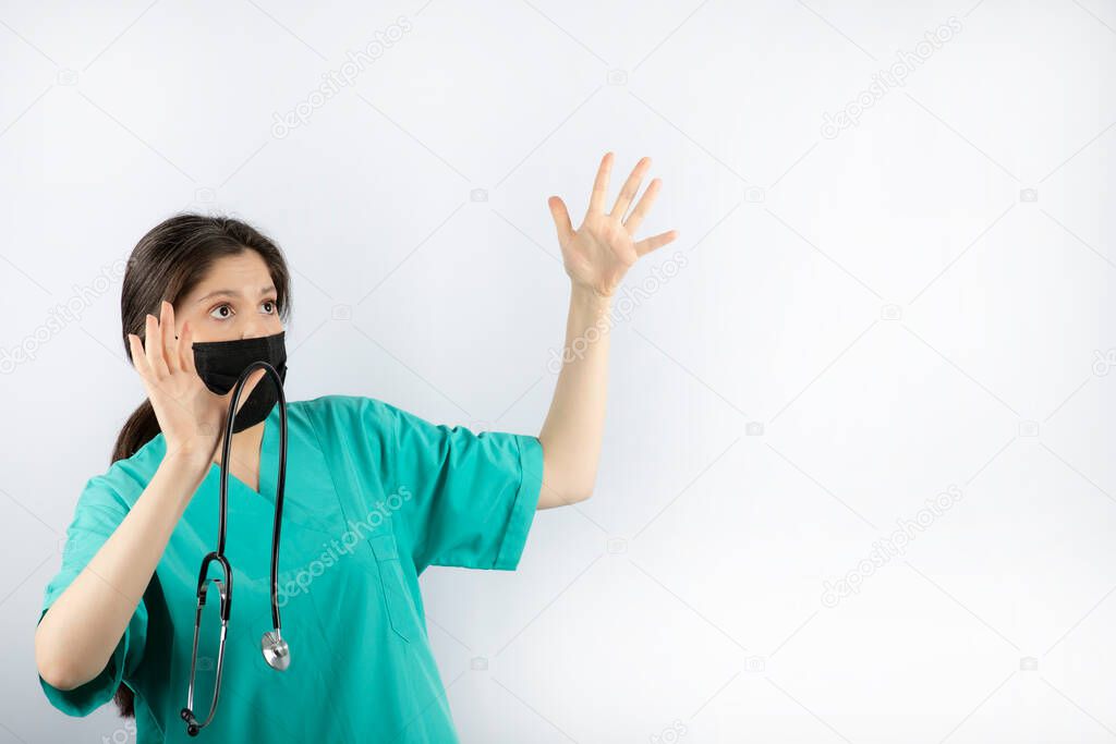 Scared young nurse holding her hands up and hold stethoscope