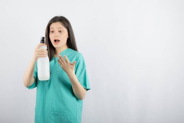 Dezenfektan şişesine bakıp el hareketi yapan genç bir hemşire.