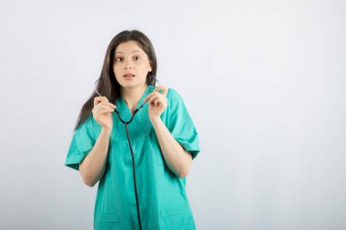 Stetoskop tutan ve kameraya bakan şok olmuş genç bir tıp çalışanı.