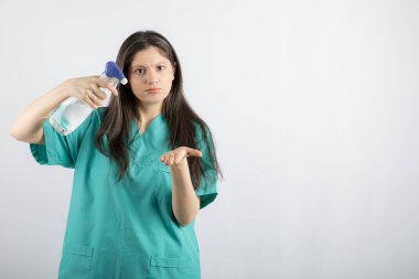 Dezenfektan tutan genç ve güzel hemşire kameraya bakıyor.