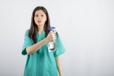 Dezenfektanlı genç, uzun saçlı hemşire kameraya bakıyor.