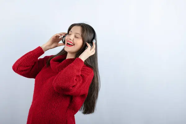 Uma jovem mulher sorridente em suéter quente vermelho ouvindo música em fones de ouvido — Fotografia de Stock