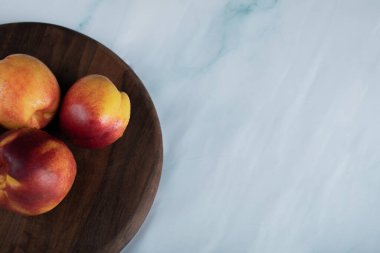 Masadaki tahtanın üzerinde kırmızı ve sarı şeftaliler