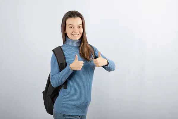 Imagem de uma jovem modelo sorridente com uma mochila mostrando os polegares para cima — Fotografia de Stock