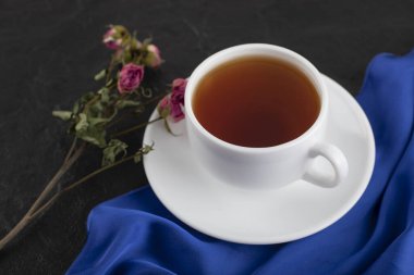 Siyah arka planda bir fincan sıcak çayla kurumuş güller.