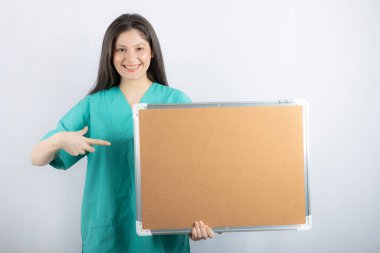 Gülümseyen sağlık çalışanı tahtayı tutuyor ve parmağıyla işaret ediyor.