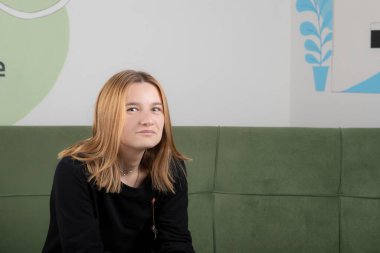 Kanepede oturan ve kameraya bakan güzel bir genç kadının portresi.