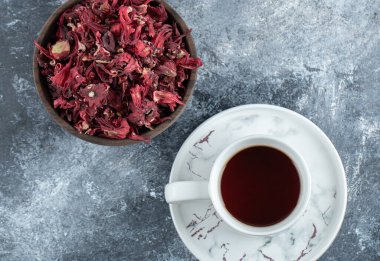 Bir fincan çay ve mermer arka planda kurutulmuş taç yaprakları.