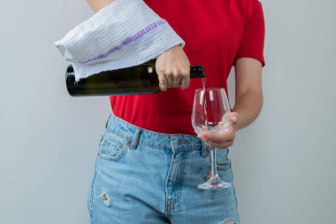 Kırmızı tişörtlü genç kız elinde bir şişe şarap ve bir bardak tutuyor.