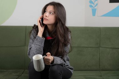 Genç kız elinde kahve tutuyor ve biriyle konuşuyor.