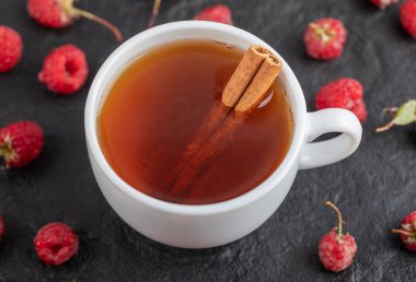 Bir fincan çay ve siyah arkaplanda taze ahududu.