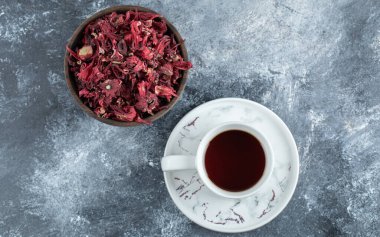 Bir fincan çay ve mermer arka planda kurutulmuş taç yaprakları.