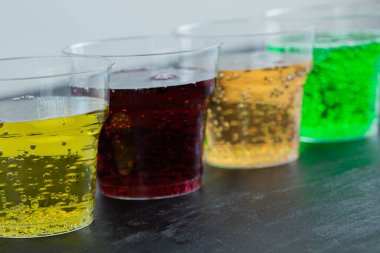 Siyah arka planda plastik bardaklarda renkli içecekler.